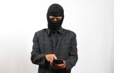 Siyah kar maskesi takan ve takım elbiseli bir adam beyaz arka plana karşı akıllı telefon kullanıyor. Güvenlik, suç veya çevrimiçi tehdit kavramı.