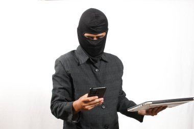 Maskeli ve takım elbiseli bir hırsız, dizüstü bilgisayar ve akıllı telefon tutuyor..