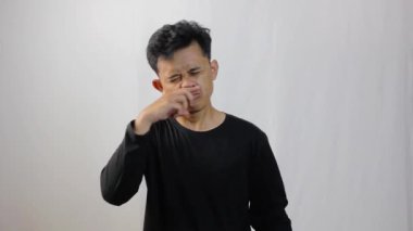 Siyah uzun kollu tişört giyen Asyalı adam gripten hasta ve beyaz arka planda parmaklarıyla kaşınıyor.