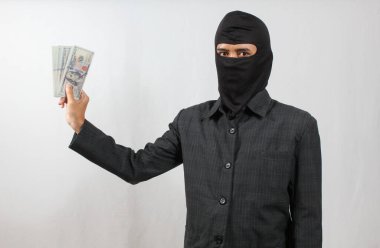 Maske takan ve siyah takım elbiseli bir hırsız beyaz arka planda izole edilmiş bir dolar fanı tutuyor.