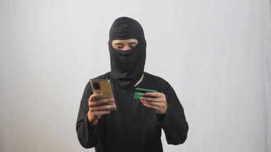 Çalıntı kredi kartı ve telefon kullanarak siber suçlar, kimlik hırsızlığı ve dijital çağ güvenlik tehdidi içeren online dolandırıcılık faaliyetleri yapan maskeli bir bilgisayar korsanı.