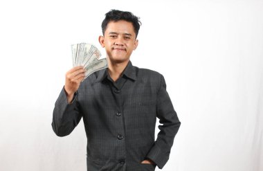 Spor ceketli bir adam elinde 100 dolarlık banknotlar tutarken kendine güvenerek gülümsüyor.