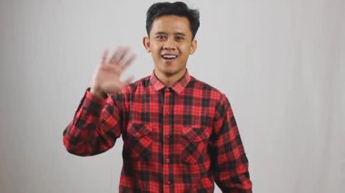 Asyalı bir adam el sallıyor. Veda ediyor. Soyutlanmış beyaz bir arkaplanı selamlıyor.