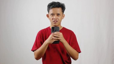 Kırmızı t-shirt giyen Asyalı bir adam konuşma pratiği için akıllı telefon kayıt sesi tutuyor.