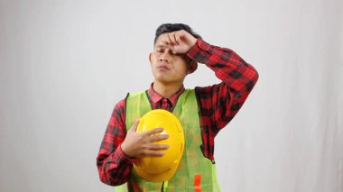 Elinde kask tutan yorgun bir inşaat işçisi alnındaki teri eliyle siler..