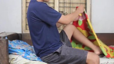 Asyalı bir adam yatağa doğru yürür. Vücudunu çiçeklerle örterek huzur içinde dinlenir.