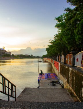 Endonezya, Solo - 15 Aralık 2025: Bir adam mavi gökyüzü günbatımının tadını çıkarırken su deposunun kenarında balık tutuyor..