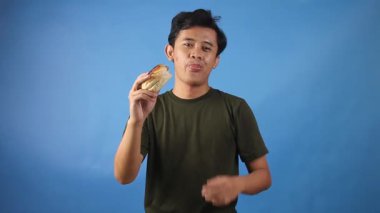 Asyalı bir adam hamburgeri açken mavi arka planda baş parmağını kaldırıyor.