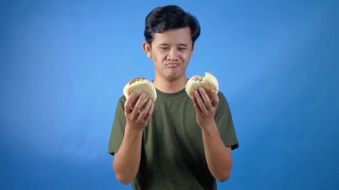 Asyalı adam elinde iki hamburger tutuyor ve onları açgözlülükle yemeyi seçiyor.