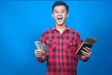 Tasarruf defteri ve mavi arka planda izole edilmiş bir miktar para gösteren mutlu Asyalı adam.