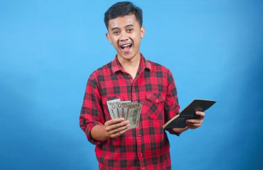 Heyecanlı Genç Adam Mutlulukla Para Gösterir ve kitaplarını saklar Mavi Arkaplan