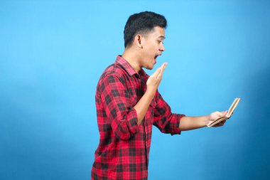 Asyalı adam mavi arkaplanda izole edilmiş tasarruf defterindeki dengeyi görünce şok oldu