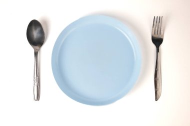 Beyaz arka planda mavi plastik tabak, kaşık ve çatal izole edilmiş. Minimalist ev çatal bıçak takımı.