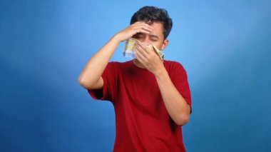 Kırmızı tişörtlü Asyalı adam mavi arka planda midesi bulanıyor.