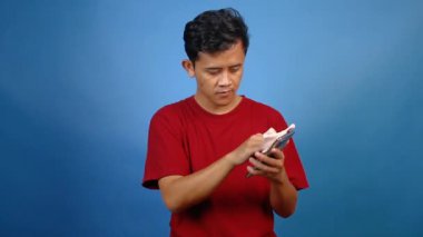 Asyalı adam mavi arkaplanda mikrofiber bez ile akıllı telefon ekranını temizliyor.