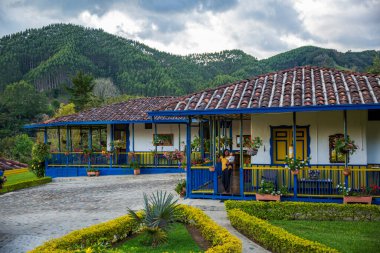 Salento, Kolombiya 'daki renkli bir evin önünde, arka planda yemyeşil tepeler ve uzun ağaçlarla birlikte gülen bir anne ve çocuk olarak neşeli bir an..