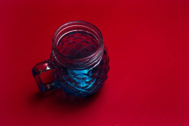 Kırmızı arkaplanda meyve suyu için mavi cam bardak yakın plan.