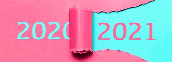 Happy new year, new start, new page of life; resolution concept. Text of 2021 on cyan background in hole of torn pink paper with text of 2020.
