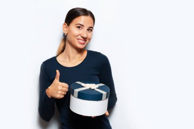 Beyaz arka planda bir hediye kutusu tutan genç bir kızın stüdyo portresi. Başparmak gösteriliyor.