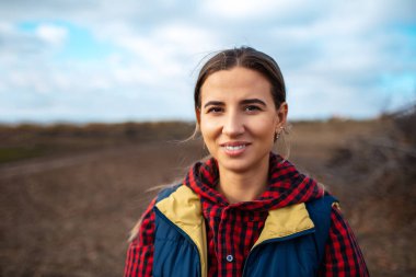 Gökyüzü ve tarlanın bulanık arka planında gülümseyen genç bir kızın açık hava portresi.