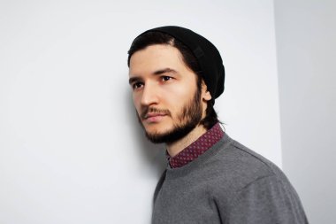 Beyaz arka planda genç bir adamın stüdyo portresi. Gri kazaklı ve siyah şapkalı adam.. 