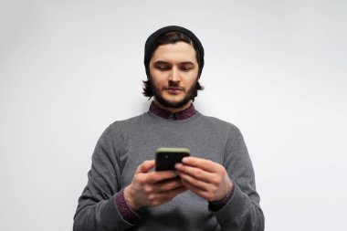 Beyaz arka planda akıllı telefon kullanan genç adamın stüdyo portresi.