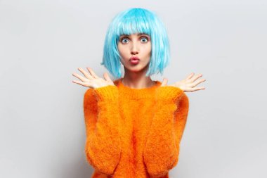 Mavi kısa saçlı komik genç kızın stüdyo portresi öpücük yolluyor, beyaz arka planda turuncu süveter giyiyor..