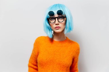 Kısa saçlı, hippi güneş gözlüğü takan ve beyaz arka planda turuncu süveter giyen şık bir kızın stüdyo portresi..