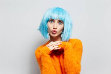 Turuncu kazaklı mavi saçlı genç kızın stüdyo portresi, beyaz arka plana öpücük yolluyor..