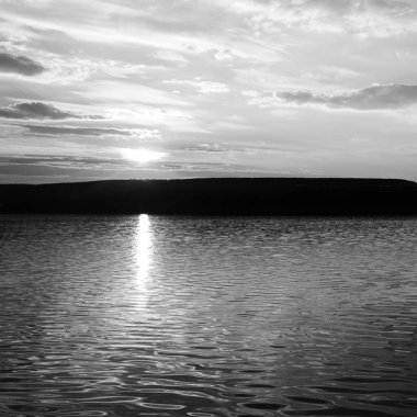 Gün batımının karanlık manzarası gölde yansıyor. Siyah beyaz fotoğraf.