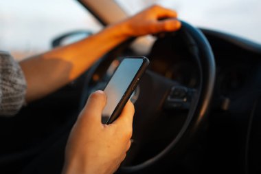 Elinde akıllı telefonuyla arabayı süren erkek elleri yakın plan..