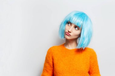 Stüdyo portresi mavi saçlı, beyaz arka planda turuncu süveter giyen komik bir kız.. 