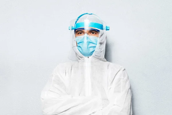 Portrait of doctor man with crossed arms, wearing PPE suit against coronavirus and covid-19, on the background of white textured wall.