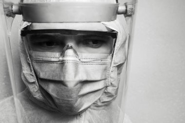 Gri duvarda, koronavirüs ve covid-19 'a karşı PPE kıyafeti giyen bir doktorun siyah beyaz portresi. Salgın konsepti.