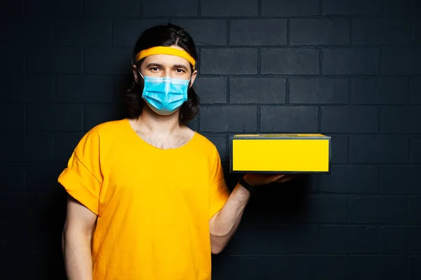 Retrato Jovem Entregador Segurando Uma Caixa Amarela Usando Máscara Médica — Fotografia de Stock