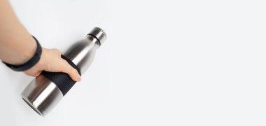 Beyaz arka planda paslanmaz termo su şişesini tutan kadın elinin fotokopi alanı ile yakın çekimi. Panoramik pankart konsepti.