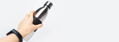 Çelik termo su şişesini, beyaz arka planda fotokopi alanı olan kadın elinin yakın çekimi. Panoramik pankart konsepti.