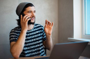 Akıllı telefondan konuşan, dizüstü bilgisayarla çalışan genç adamın portresi..