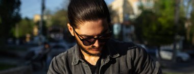 Panoramik pankart görünümü; güneş gözlüğü takan genç ciddi bir adamın portresi.