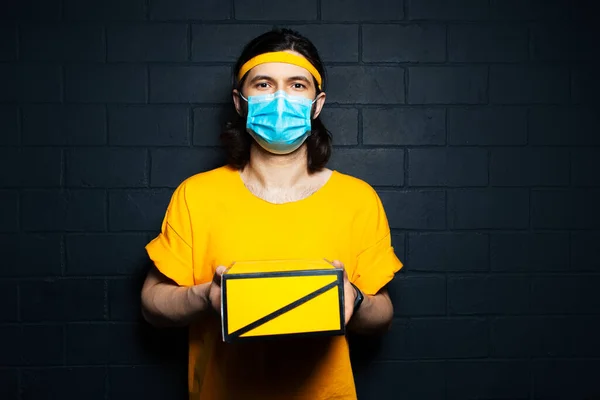 Retrato Jovem Entregador Dando Uma Caixa Amarela Vestindo Máscara Médica — Fotografia de Stock