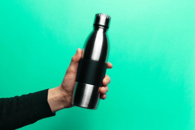 Stüdyo görüntüsü, yeşil zemin üzerinde tekrar kullanılabilir çelik termo şişe tutan erkek eli.. 