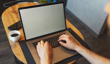 Erkek ellerinin bilgisayar klavyesinde daktilo yazarken üst görünümü, dizüstü bilgisayarda çalışan adam, akıllı telefon ve kahve fincanı ahşap masada..