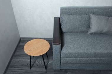 Yuvarlak ahşap masa ve gri kanepede, gri lamine zeminde dokulu duvarlar var..