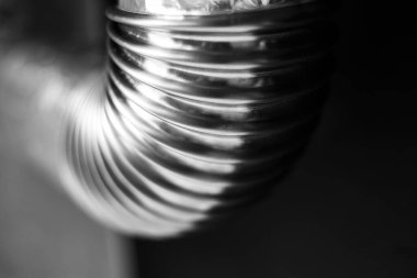 Siyah beyaz fotoğraf; siyah-gri arka planda yuvarlak köşeli paslanmaz boru yakın plan.