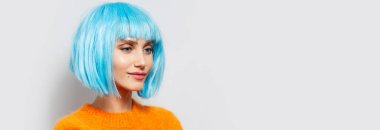 Stüdyoda mavi saçlı, beyaz arka planda turuncu süveter giyen güzel bir kızın portresi. Kopya alanı ile panoramik pankart görünümü.