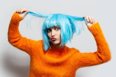 Stüdyo portresi mavi saçlı, beyaz arka planda turuncu süveter giyen komik bir kız..