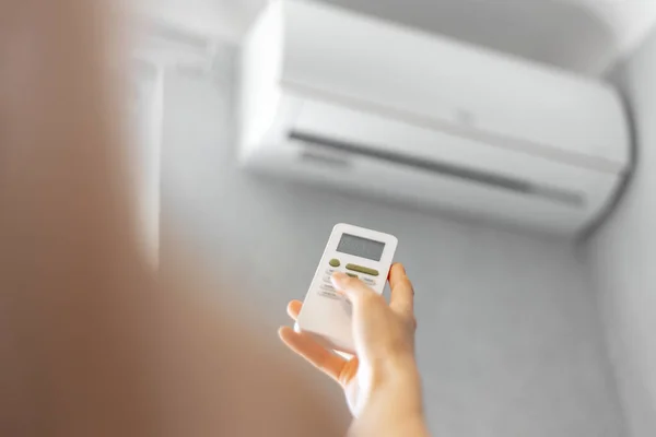 Close-up of female hand adjusting air conditioner with remote control. Summer concept.