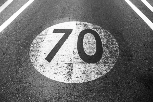 アスファルト道路上に描かれた時間あたり70キロと古いみすぼらしい速度制限記号の黒と白の写真 — ストック写真