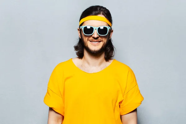 Portrait of young smiling man in yellow wearing sunglasses on textured background of grey.