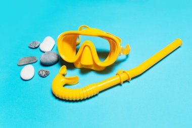 Close-up of yellow diving mask with snorkel near stones on blue background.